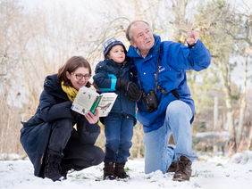Eine Familie mit Kind beobachtet Vögel im Schnee.