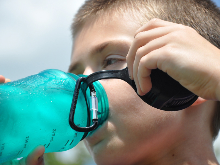 Ein Junge trinkt aus einer blauen Trinkflasche.
