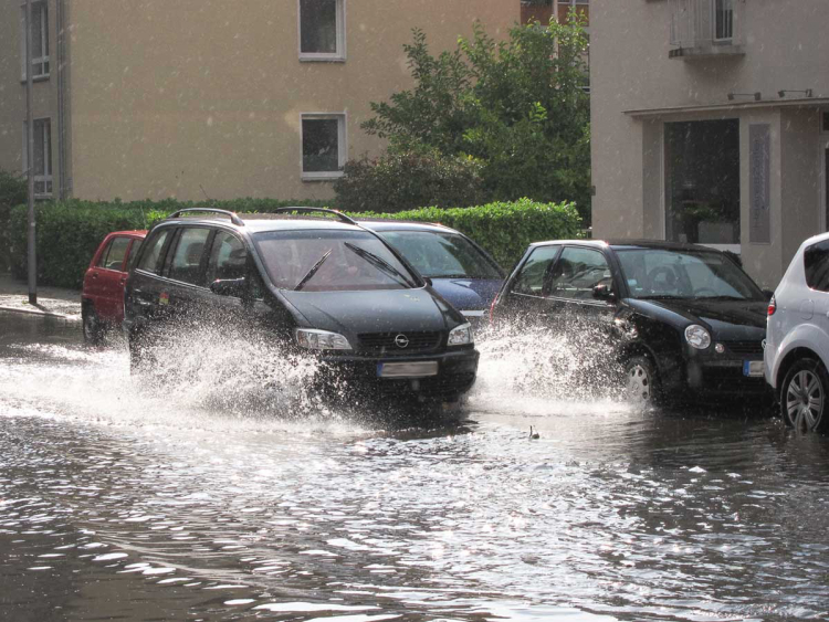 Auto fährt durch Straße mit Hochwasser.
