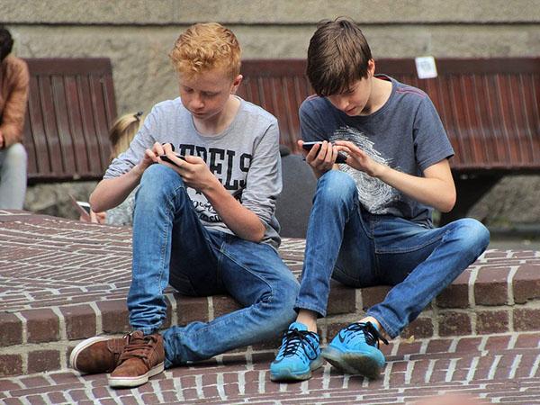Zwei Jungen mit Smartphones an der Straße sitzend.