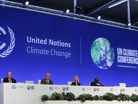 Personen auf einem Podium vor dem Logo der Weltklimakonferenz in Glasgow