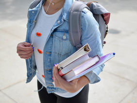 Eine Person trägt Ordner und Schulbücher.