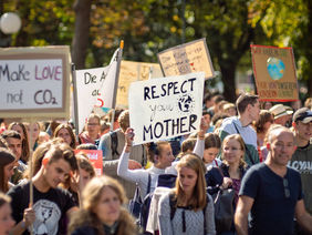 Demonstrierende Menschen mit Plakaten, darauf Slogans für den Klimaschutz wie "Make Love not CO2"
