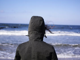 Eine Person mit einer Kapuze blickt auf das Meer
