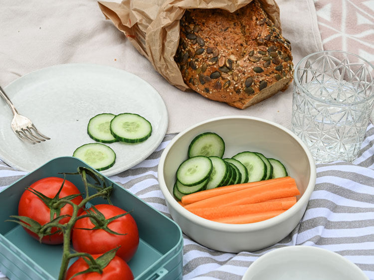 Gemüse in Brotdosen, ein Teller und ein Brot auf einer Picknickdecke