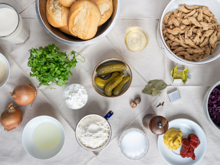Gewürzgurken, Mehl, Stärke, Brötchen, Gewürze, Zwiebeln, Petersilie, Rotkraut, Senf und Tomatenmark auf einem Tisch