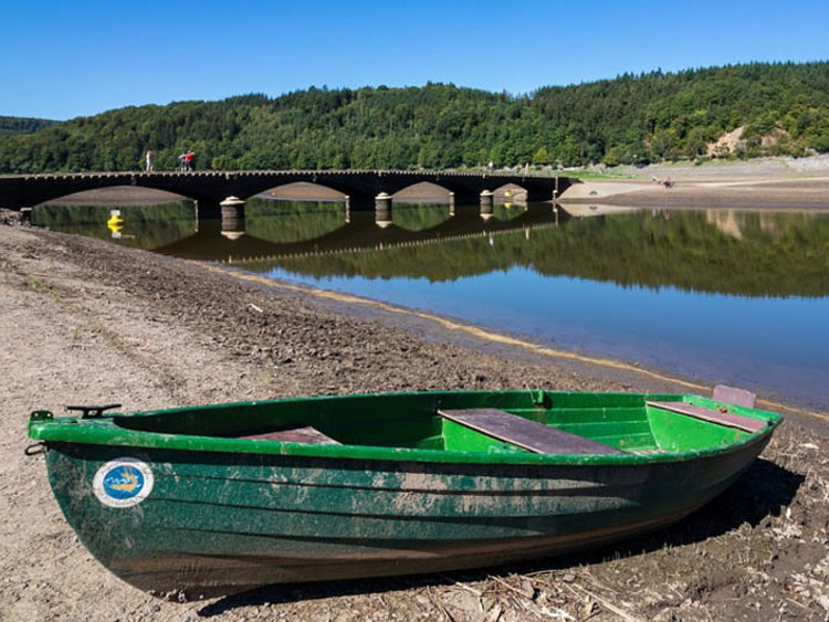 Ein grünes Boot an einem See. im Hintergrund eine Brücke über den See