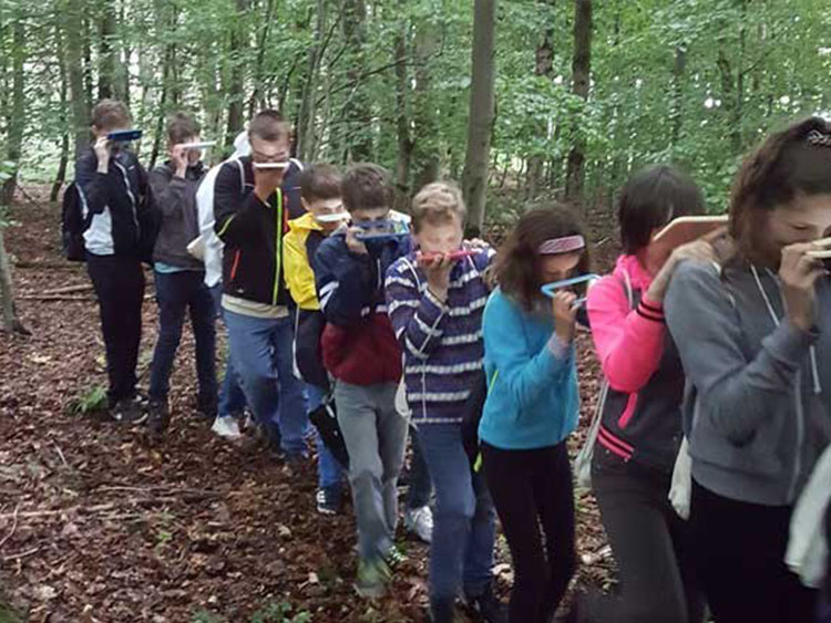 Schüler laufen mit Spiegeln vor dem Gesicht durch Wald